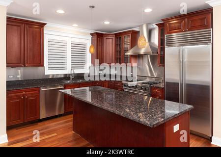 A luxury kitchen with cherry wood cabinets, stainless steel appliances, a large island, and a granite countertop. Stock Photo