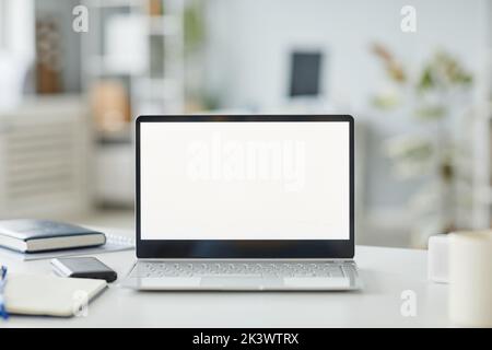 Background image of opened laptop with white screen mockup at workplace in minimal office interior white and grey tones, copy space Stock Photo