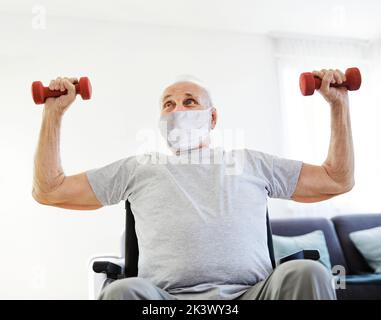 Happy senior man in wheelchair wearing protective mask exercising at home or nursing home Stock Photo