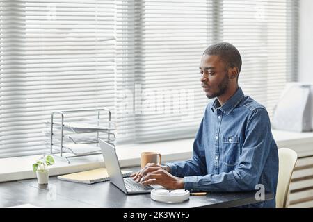 Graphic side view portrait of young black professional using laptop by window in office, copy space Stock Photo