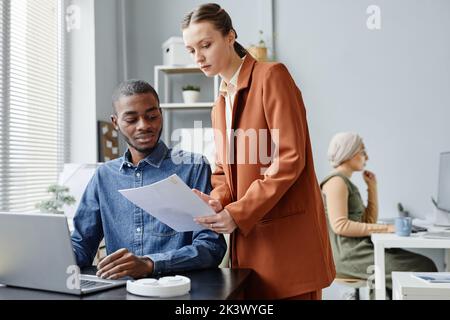 Portrait of female manager talking to young employee in office and discussing work documents Stock Photo