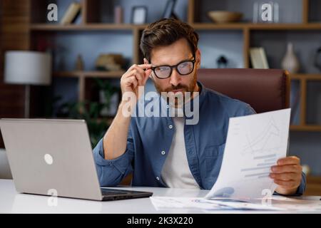 Handsome male businessman manager working behind a laptop in a stylish home office. Remote work at home. Portrait of a successful freelancer. Stock Photo