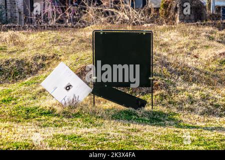 Black realtor's sign with hanging name sign partly broken off and lot number 6 sign in rough grassy vacant lot for sale - Selective focus Stock Photo