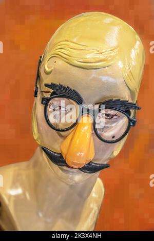 Retro mannequin head with forehead curl wearing funny costume glasses with orange nose and mustache - isolated on orange background Stock Photo