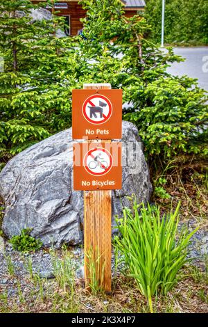 Simple wooden No Dogs No Bicycles sign with icons at roadside lookout on Alaskan Highway Stock Photo