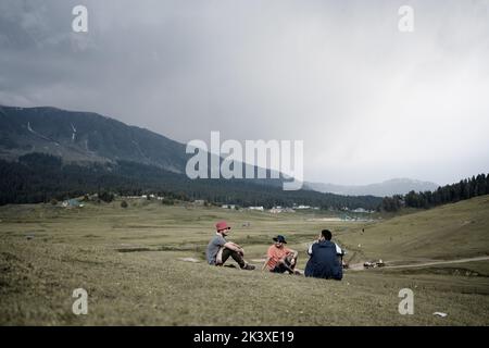 A shot of three people sitting and talking on a grass field Stock Photo
