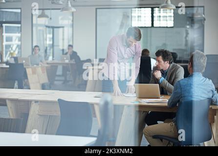 Getting down to business. Through the glass shot of a group of colleagues working together in an office. Stock Photo