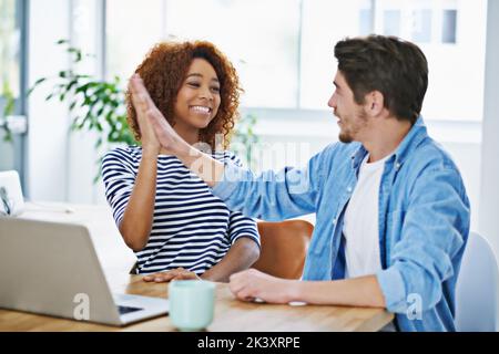 Two pair of eyes are better than one. two coworkers high giving at their desk. Stock Photo