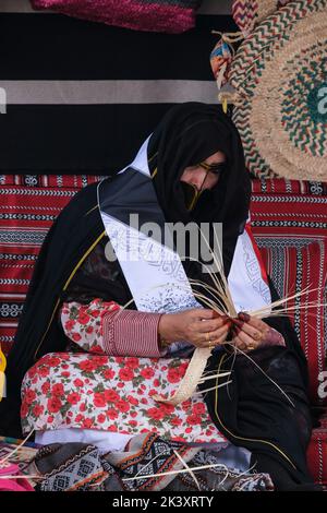 Masked Arab Woman from Abu Dhabi Wearing an Abaya Making Bands from Date palm Fiber for use in Making Traditional Straw Baskets. Stock Photo