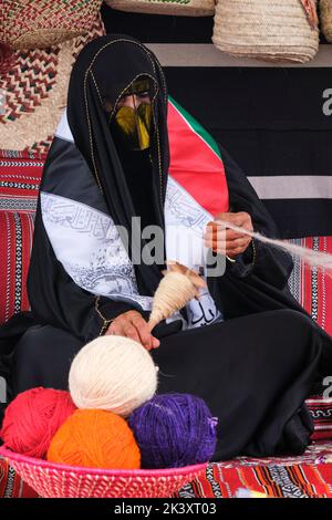 Masked Arab Woman from Abu Dhabi Wearing an Abaya at a Folklife Festival Demonstrating Traditional Handicraft Skills,  Putting Wool on to a Spindle. Stock Photo