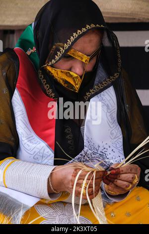 Masked Arab Woman from Abu Dhabi Wearing an Abaya Making Bands from Date palm Fiber for use in Making Traditional Straw Baskets. Stock Photo