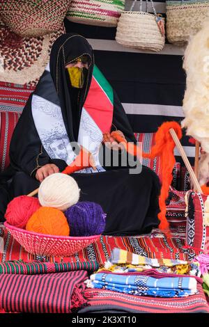 Masked Arab Woman from Abu Dhabi Wearing an Abaya at a Folklife Festival Demonstrating Traditional Handicraft Skills,  Putting Wool on to a Spindle. Stock Photo