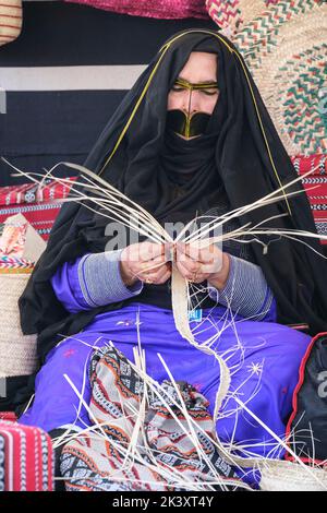 Masked Arab Woman from Abu Dhabi Wearing an Abaya Making Bands from Date palm Fiber for use in Making Traditional Straw Baskets. Stock Photo