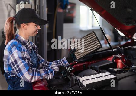 Caucasian female auto mechanic changes the engine air filter in the car. Stock Photo