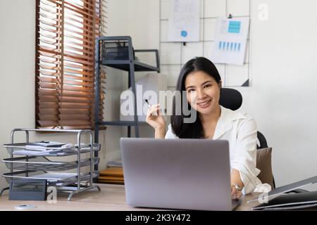 Photo of joyful nice woman using laptop and smiling while sitting at office. Stock Photo