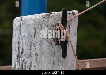 A red and white rope is tied around a cleat on a post at a wharf to keep a boat secure. Stock Photo