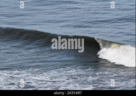 Wave crests then rolls down the face of the wave, throwing spray off the top. Stock Photo