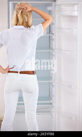 Where did all my food go. Rearview of a young woman looking in her empty fridge. Stock Photo