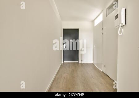 Interior of narrow corridor with telephone , radiator and many doors in white walls over lumber floor Stock Photo