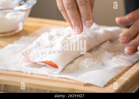 Marinated Salmon with Salt on paper tissue food grade on Wooden cutting plate by Professional hand Chef. Stock Photo