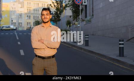 Successful hispanic business man arabic guy stands in city outdoors background of street with crossed arms thinking planning dreaming with serious Stock Photo