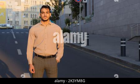 Hispanic handsome young business man arabic bearded manager worker boss leader guy entrepreneur in formal clothes stands in city street background Stock Photo