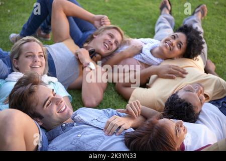 Taking a break after class. A group of young students lying on the grass on campus. Stock Photo