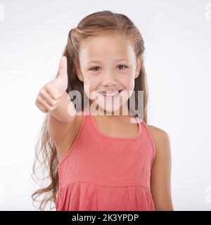 Shes so happy and carefree. Studio portrait of a cute young girl giving a thumbs-up to the camera. Stock Photo