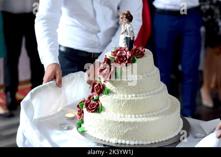 Ivory-colored wedding cake, garnet roses and groom and bride mini figurines Stock Photo