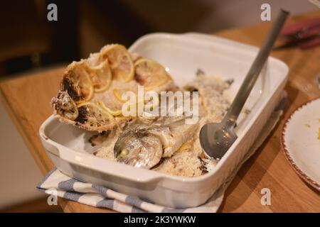 Fish in the salt crust in the oven placed in the white ceramic tray. Stock Photo