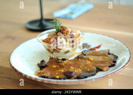 French delicacy. Bowl with baked potatoes au gratin and venison meat with flavored sauce. Stock Photo