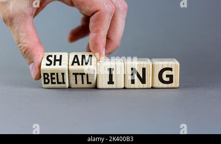 Shaming and belittling symbol. Concept words Shaming and Belittling on wooden cubes. Businessman hand. Beautiful grey table grey background. Business Stock Photo