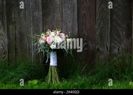 An elegant rustic wedding bouquet of selected white roses and eucalyptus foliage resting on a natural dark weathered wooden texture background. Stock Photo
