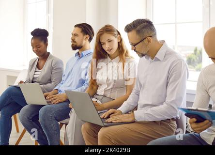 Diverse business people working on laptop computers while sitting in line in office Stock Photo