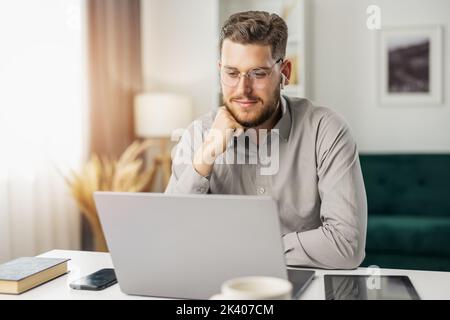 Happy young coder working with laptop from home, handsome man coding using gadgets and computer Stock Photo