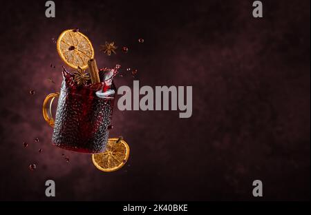 Mulled wine with splashes and flying ingredients on dark background. Copy space Stock Photo