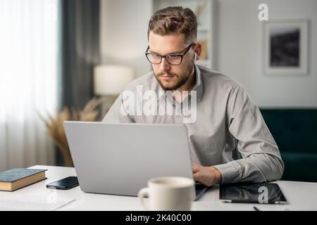 Young handsome man coding with at laptop from home, remote work, intelligent coder writing software code Stock Photo