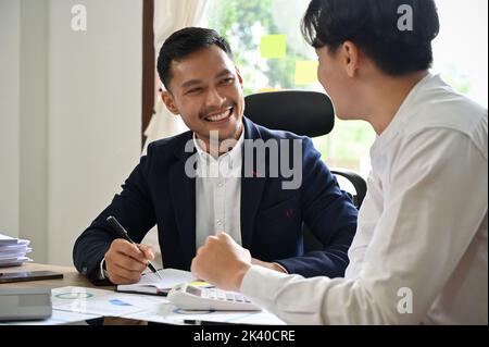 Two Asian male accountants or financial consultants working together, having a nice conversation during work. Stock Photo