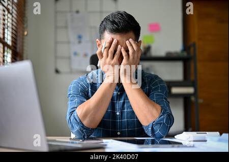 Stressed and exhausted Asian businessman or male office worker sits at his desk, suffering from his anxiety, feeling upset with his work performance. Stock Photo