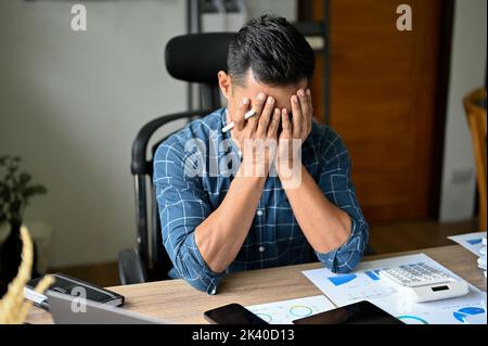Stressed Asian businessman or male business startup entrepreneur suffering from his anxiety, feeling upset with his work performance. failure, exhaust Stock Photo