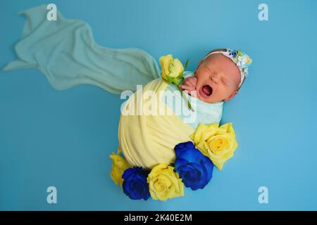 Ukrainian newborn crying in the studio patriotic blue yellow colors during the war in Ukraine 2022. A little baby, girl sleeps on isolated background Stock Photo