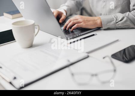 Top view of business white desk, cropped businessman typing on laptop next to paper documents and cup, office workplace Stock Photo