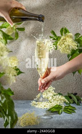 Real woman preparing Elder Fashion Royal Cocktail in Champagne glass surrounded by ingredients and bar tools on gray table surface. Refreshing drink r Stock Photo