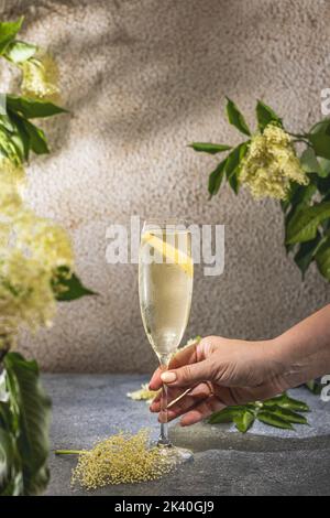 Real woman preparing Elder Fashion Royal Cocktail in Champagne glass surrounded by ingredients and bar tools on gray table surface. Refreshing drink r Stock Photo