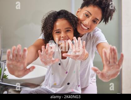 Woman, child and washing hands in bathroom, cleaning to prevent germs and virus in home. Soap, water and hygiene, girl and mom from Brazil. Teaching Stock Photo