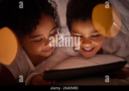 Children learning on a digital tablet while bonding in bed at night, happy and relax while streaming together. Happy girl and boy awake late, enjoying Stock Photo