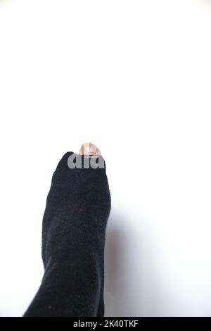 Hole in a black sock through which the big toe sticks out. White background. Upright image. Copyspace. Stock Photo