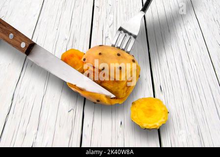 Peel prickly pears with fork and knife on white wooden table Stock Photo