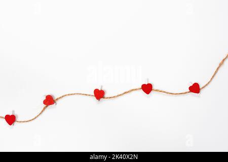 Set of wooden clothespins with red hearts held on string on white background. Concept of greetings to St. Valentine, day of all lovers. Copy Space for Stock Photo