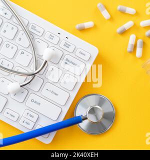 Doctor diagnoses design concept - stethoscope with computer keyboard and capsule pill on yellow background. Stock Photo